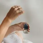 A woman holding a dropper bottle of skincare serum over her hand in clean flat lay style
