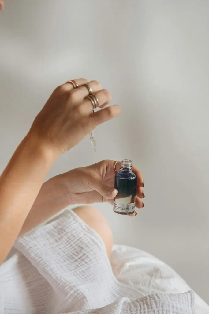 A woman holding a dropper bottle of skincare serum over her hand in clean flat lay style